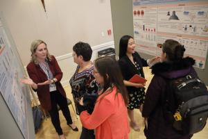 Graduate students explain their research posters to faculty and staff