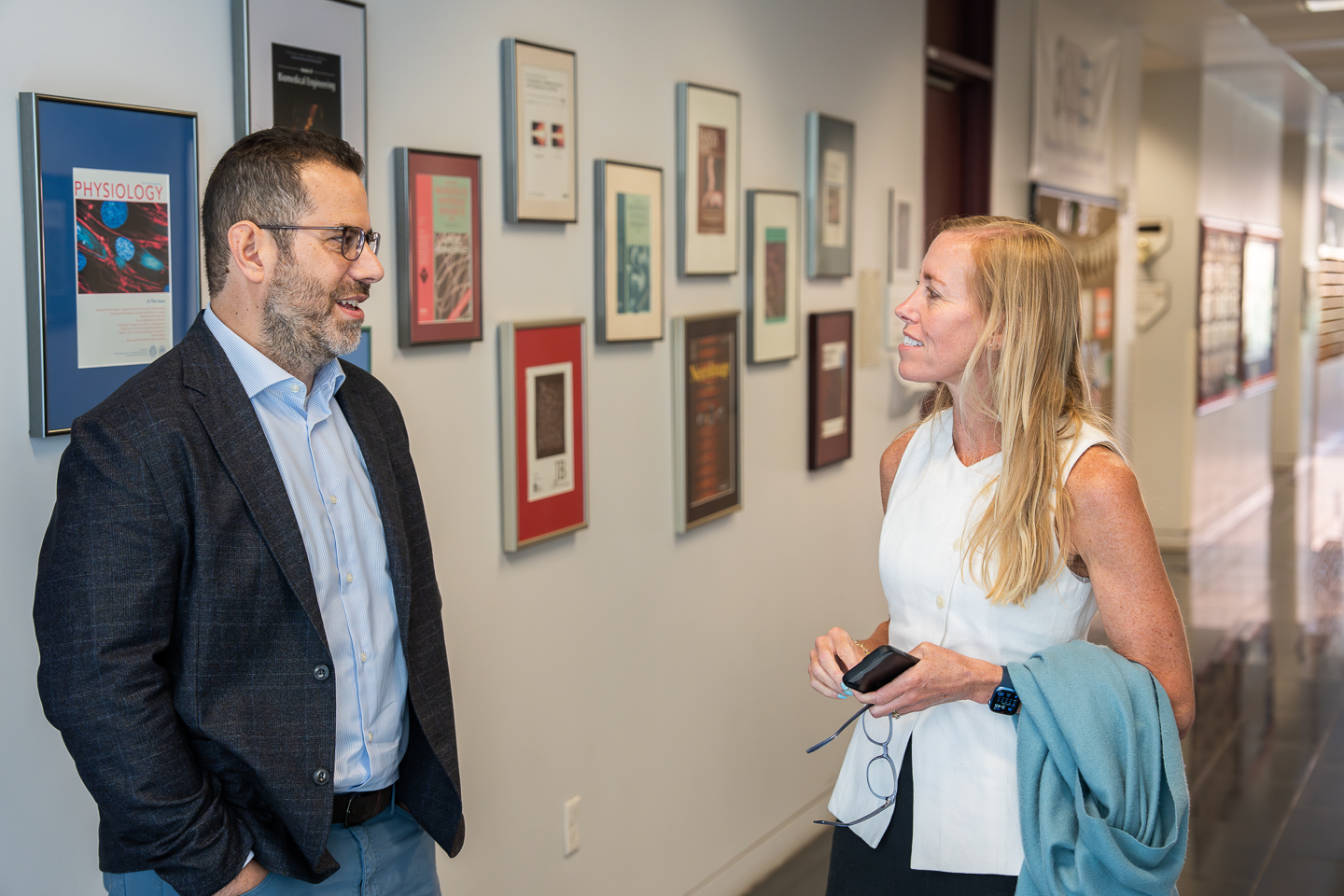 A man and a woman, Francesco Viola and Shayn Peirce-Cottler, converse in an academic building hallway.