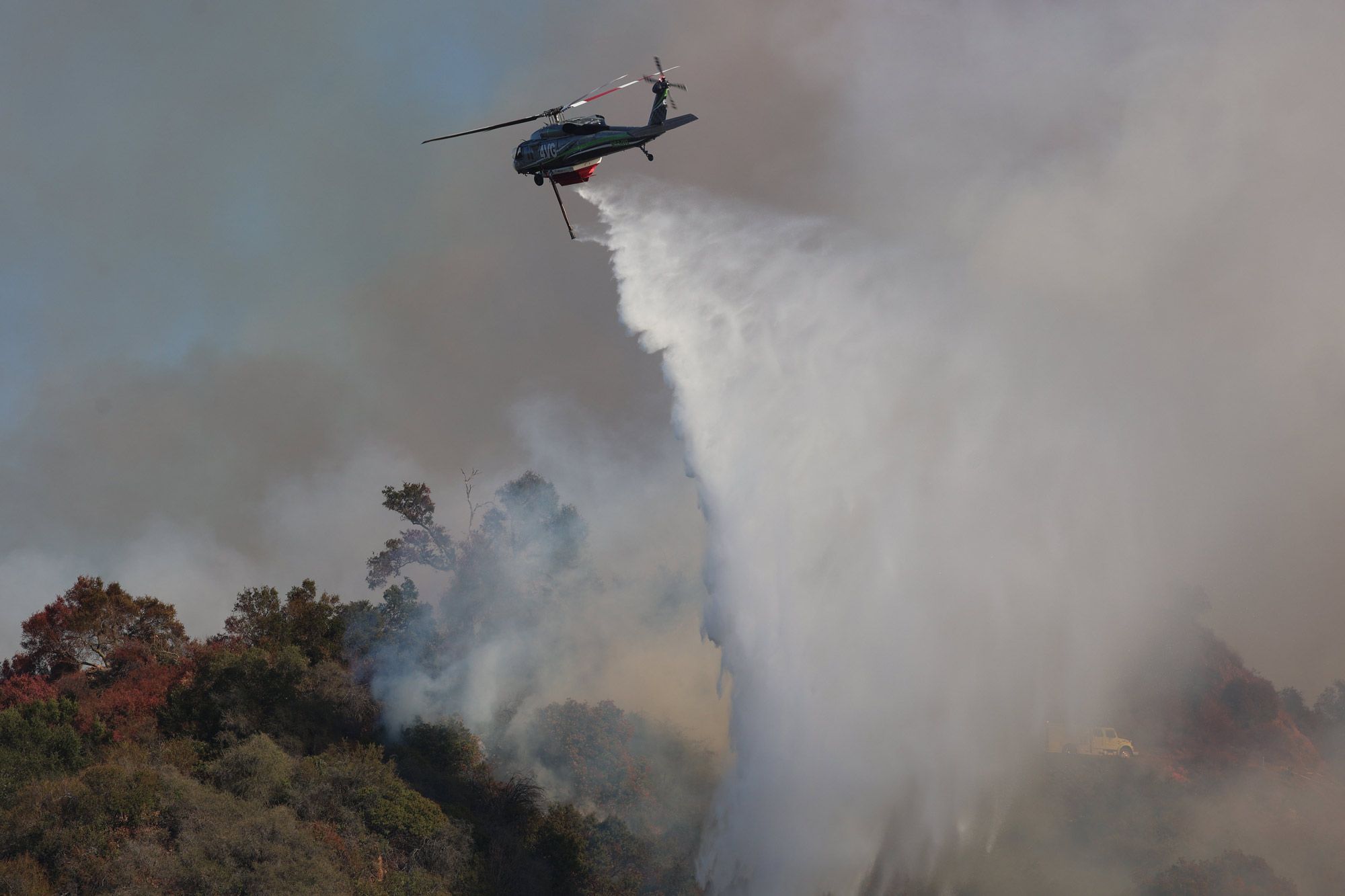 A helicopter drops water on a burning mountainside in California.