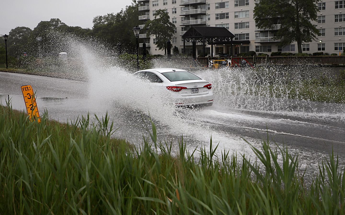 Water sprays from a car's wheels as it drives through a flooded road