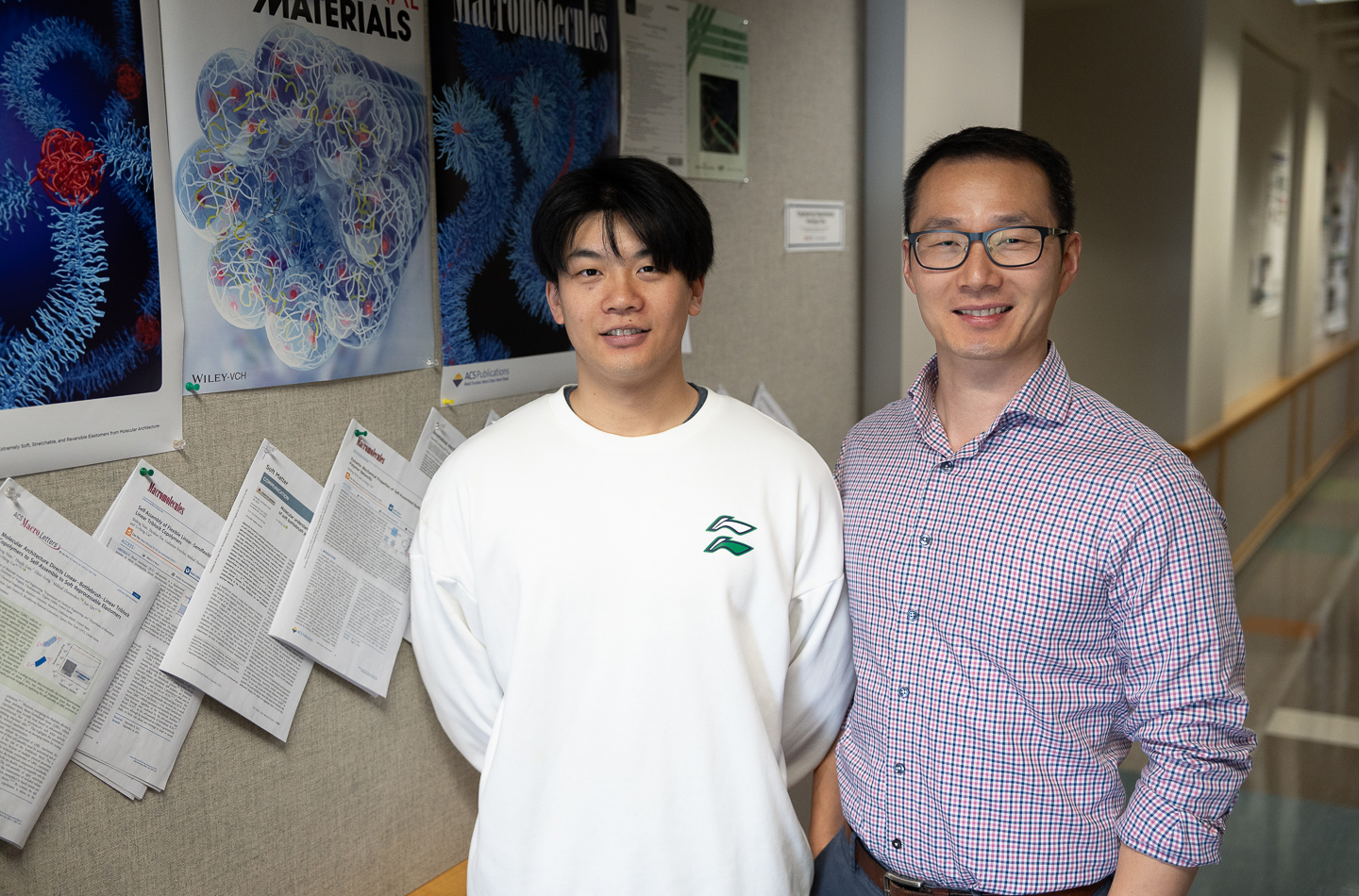 Two men posing for a photo in a hallway in front of posters