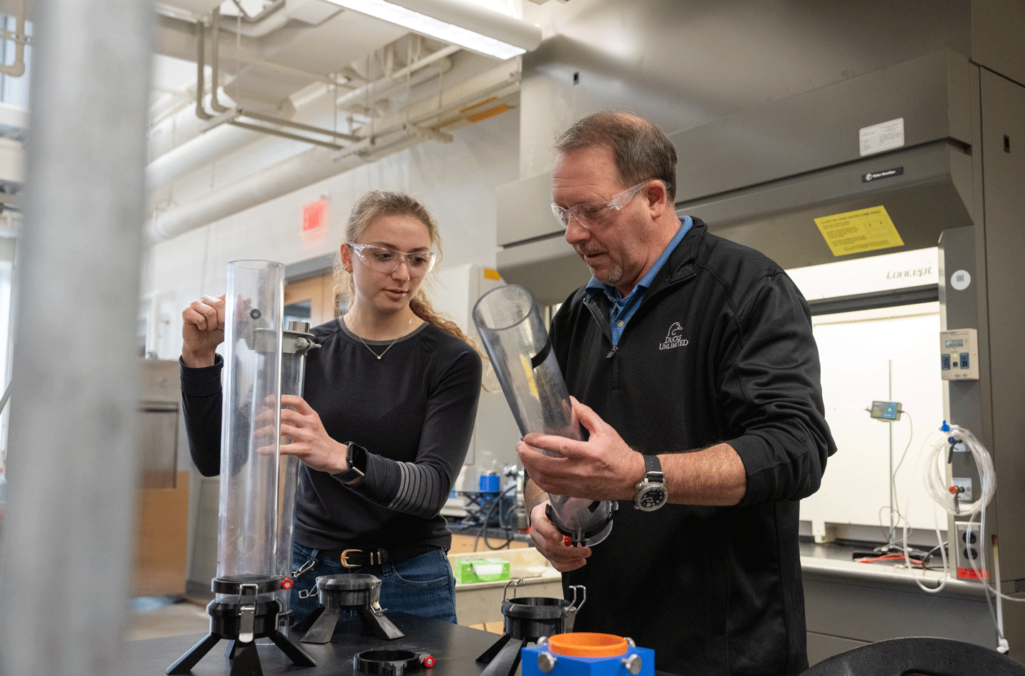 Two people in a chemical engineering lab working on a tubular device designed to test the explosivity of dust.