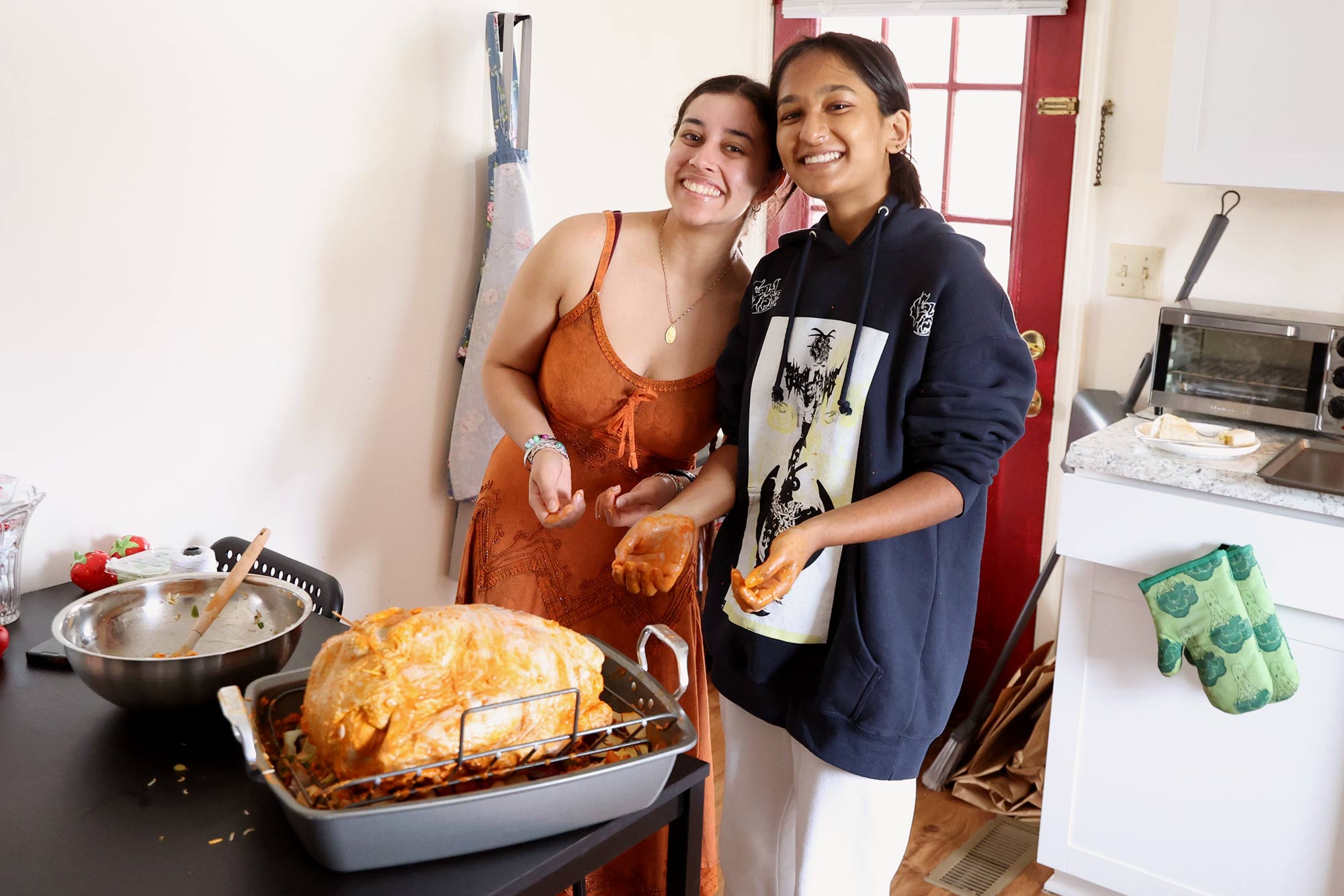 Two smiling young women in a kitchen preparing a turkey with orange-colored tandoori seasoning