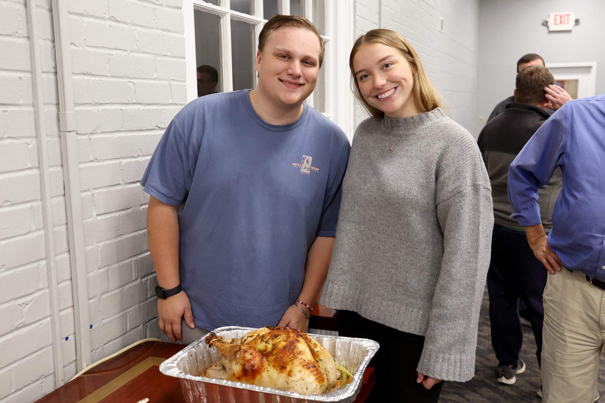 A young man and a young woman posing with a cooked turkey at a buffet dinner.