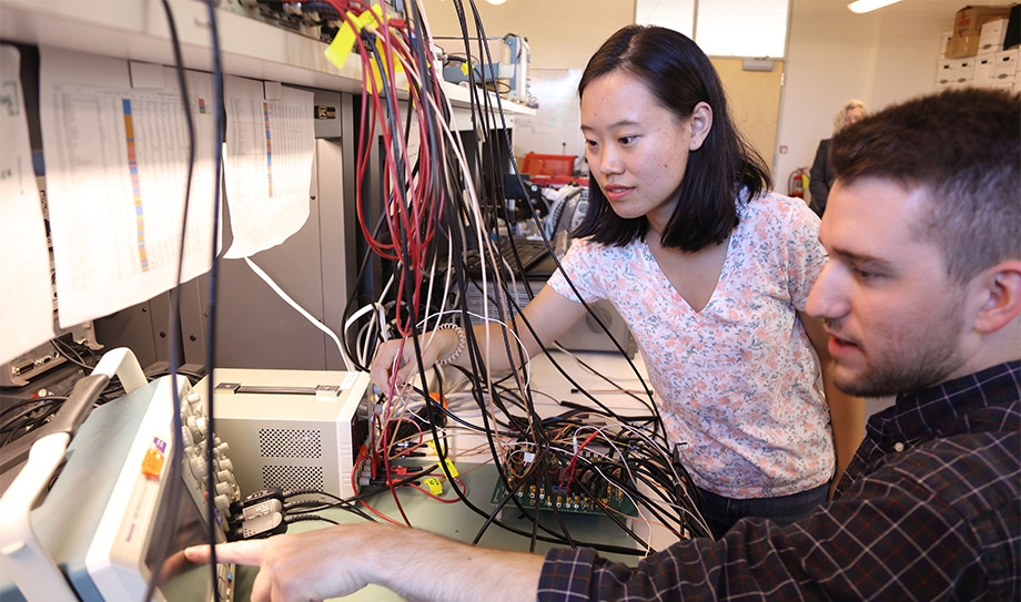 Peng Wang and Daniel Truesdell working with machines