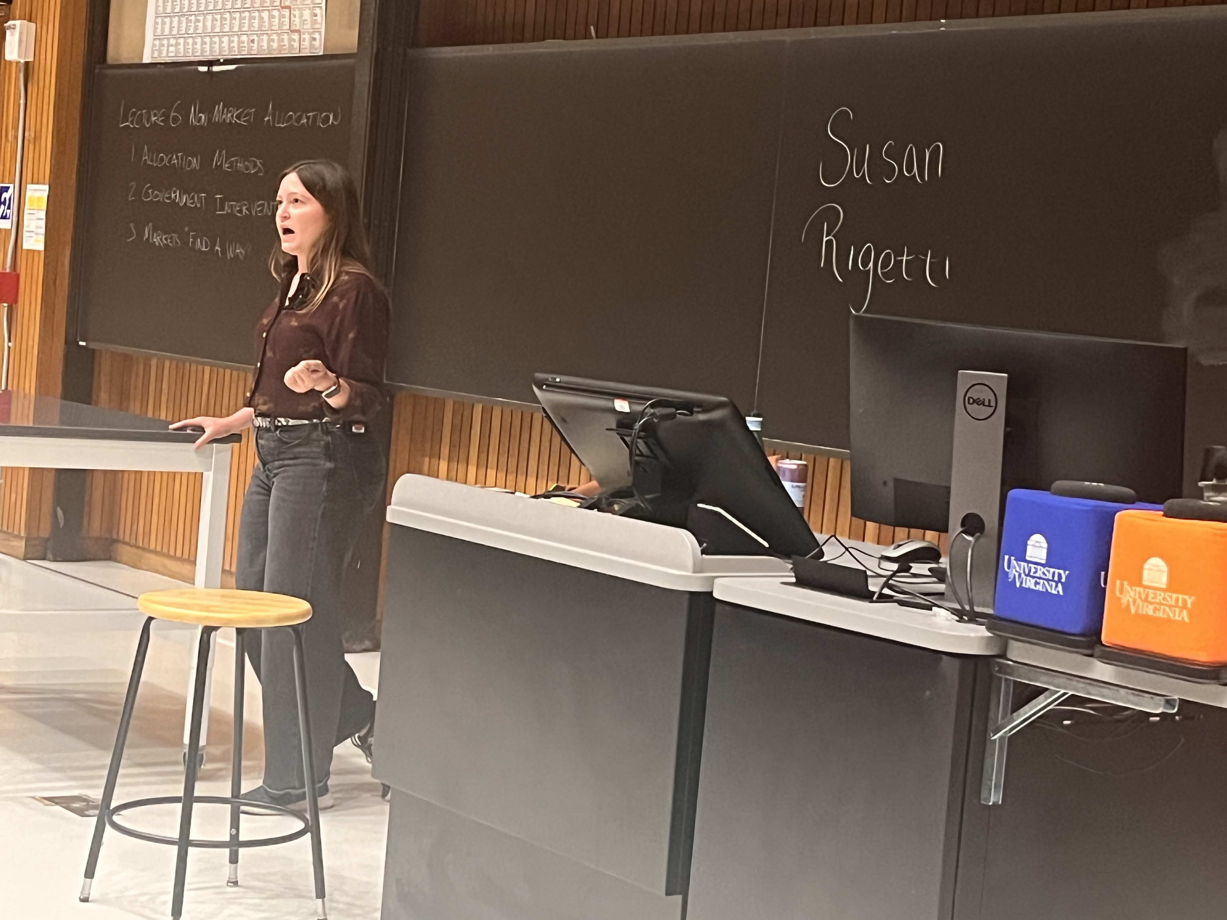A woman standing in front of a classroom chalkboard gives a lecture.