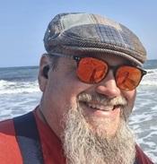 Image of Jeff wearing sunglasses and a hat on the beach