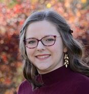 woman wearing glasses and a purple sweater smiling outside