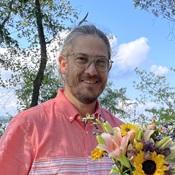 Image of man smiling outside wearing glasses holding flowers