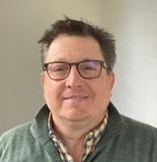 man in greenish grey sweater and glasses smiling