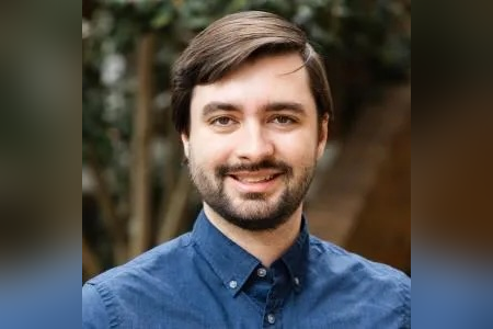 W. Streit Cunningham head-and-shoulders portrait outdoors, wearing a blue button-down shirt and facing the camera. The background is softly blurred with trees and warm-toned foliage.