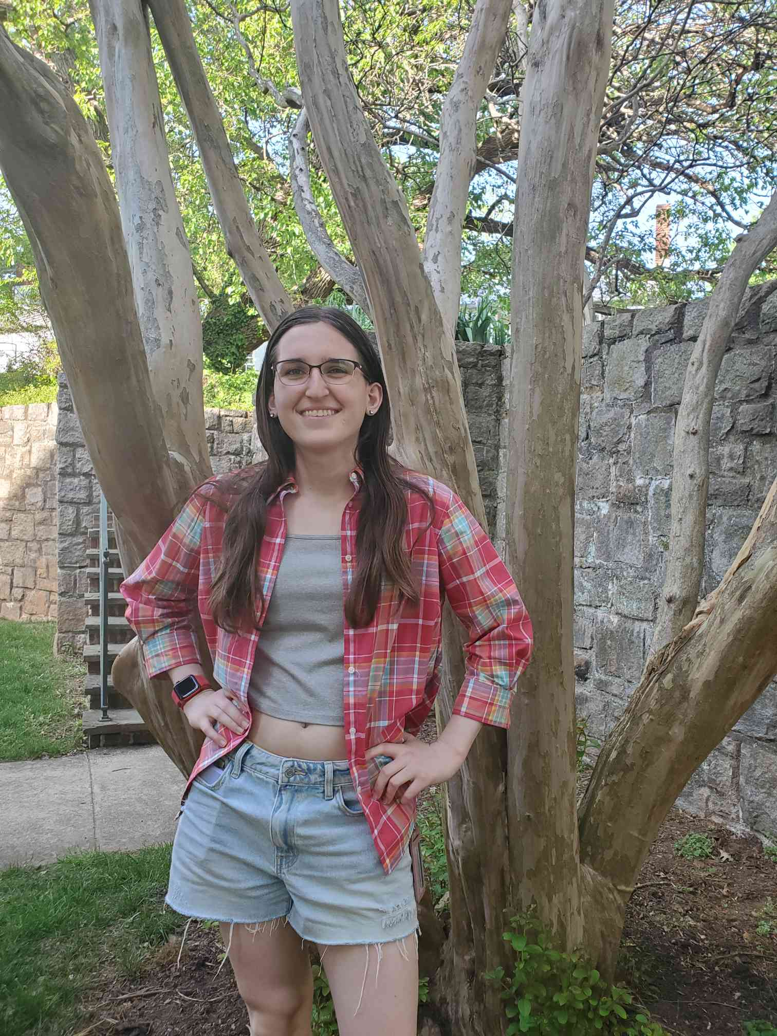 A student stands in front of a tree with her hands on her hips