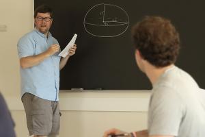 classroom setting showing male professor in front of a chalkboard while he lectures