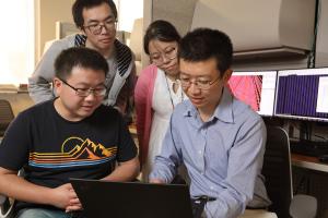 Bi-Cheng Zhou and students look at a laptop