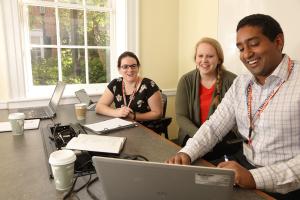 Accelerated master's program students look at a laptop together in a meeting room