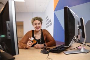 A student in the Human Systems Engineering Lab seated at a computer, holding a medication bottle