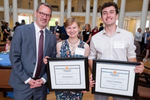 Three people, two holding award certificates