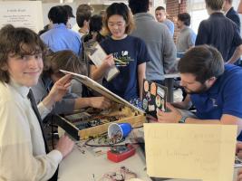 A student smiling at the camera while team members work on a project