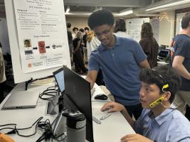 Two students by a table with a computer, one wearing a custom sensor as a headset