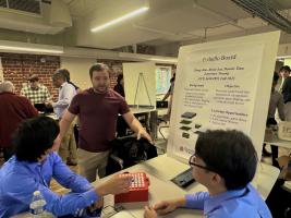 Students gathered around a table with a "E-thello board" poster 