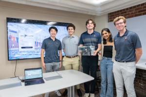 Department of Electrical and Computer Engineering capstone students stand in the lab with the box-shaped device they created to read the force applied during swim starts..