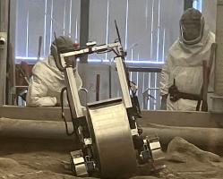 A robot in the foreground with two people wearing PPE behind the robot.