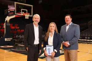 A woman holding an award standing between two men on a basketball court