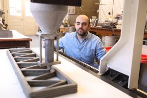 A man watching a 3D concrete printer make a sample building component
