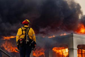 Photo of a firefighter watching black smoke and flame in the background