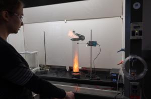 A female student watching a contained explosion in a tube behind a fume hood screen