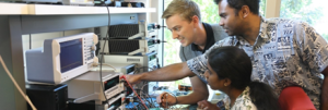 Three students working at a lab bench with electronic equipment