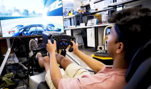 Student sitting at the wheel in a driving simulator with virtual road displayed on the simulator's monitor.
