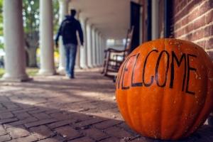 A pumpkin with the word "Welcome" painted on it in front of a Lawn room