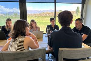 A group of people at a conference table against a backdrop of mountain seen in the distance through picture windows.