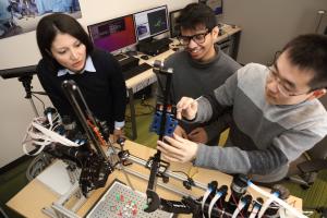 A female professor and two male grad students work on a medical robot.