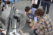 Two men kneeling in front of robot to inspect it.