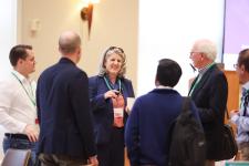 Attendees network and converse during UVA Link Lab Research Day, with a woman in a navy blazer speaking to a small group in a conference setting.
