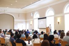 Audience listens to a speaker presenting at UVA Link Lab Research Day in a bright conference room with large arched windows.