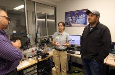 Woman stands next to man talking to second man next to a surgical assisting robot