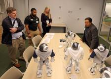 A man stands next to a table of NAO robots talking to 3 people