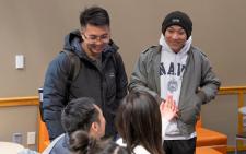 Two students standing, talking and laughing with seated students