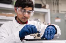 A man wearing a white lab coat and blue gloves works in a catalysis lab 