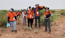 A group of people in orange shirts in the New Mexico desert holding parts of a rocket.