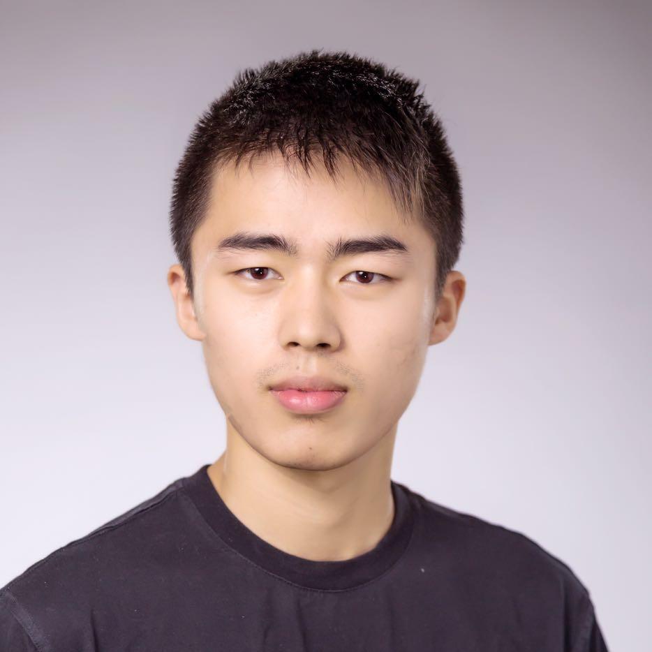 man wearing black shirt with dark hair smiling against light background.