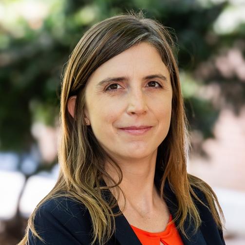 woman wearing orange shirt with navy blue jacket smiling outside