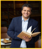 Photo of Dr. Surampudi holding a book in front of a chair and chessboard