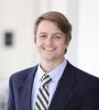 Man Stands in 3-piece suite stands smiling with blurred background