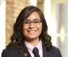 person with long brown wavy hair wearing glasses smiling outside