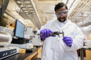 Graduate student in a lab coat measures a sample in the Opila Lab