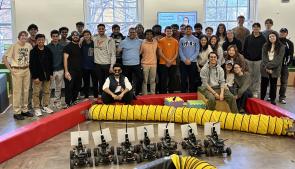 Students of the F1/10 Autonomous Racing class Fall 2024 stand on race course with instructor, Madhur Behl behind their F1/10 race cars 